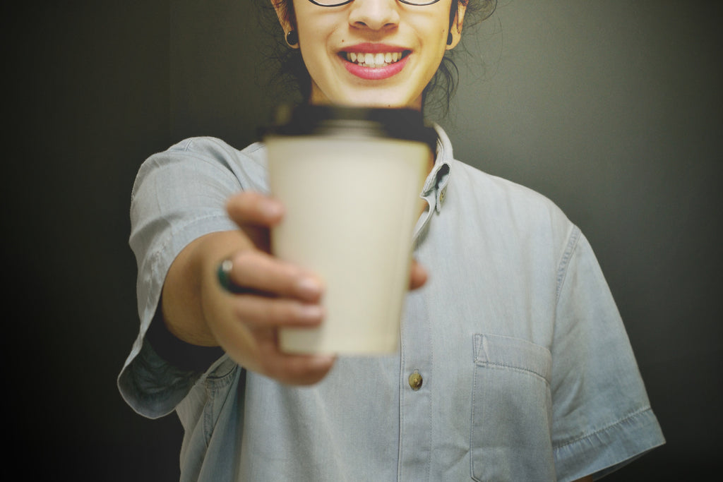 A young woman holding a paper cup of coffee in front of her.