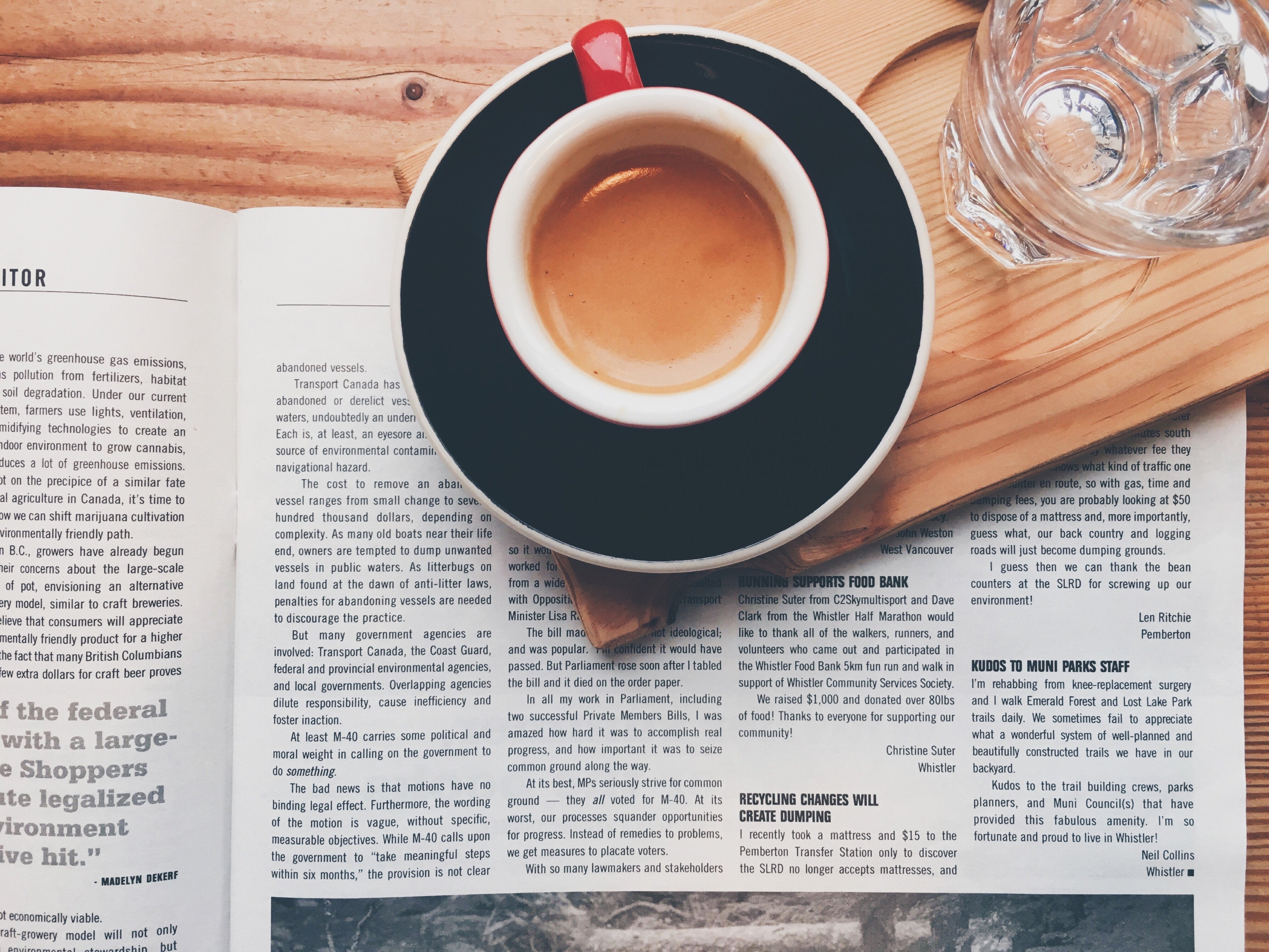A cup of espresso with a glass of water sitting on a newspaper.