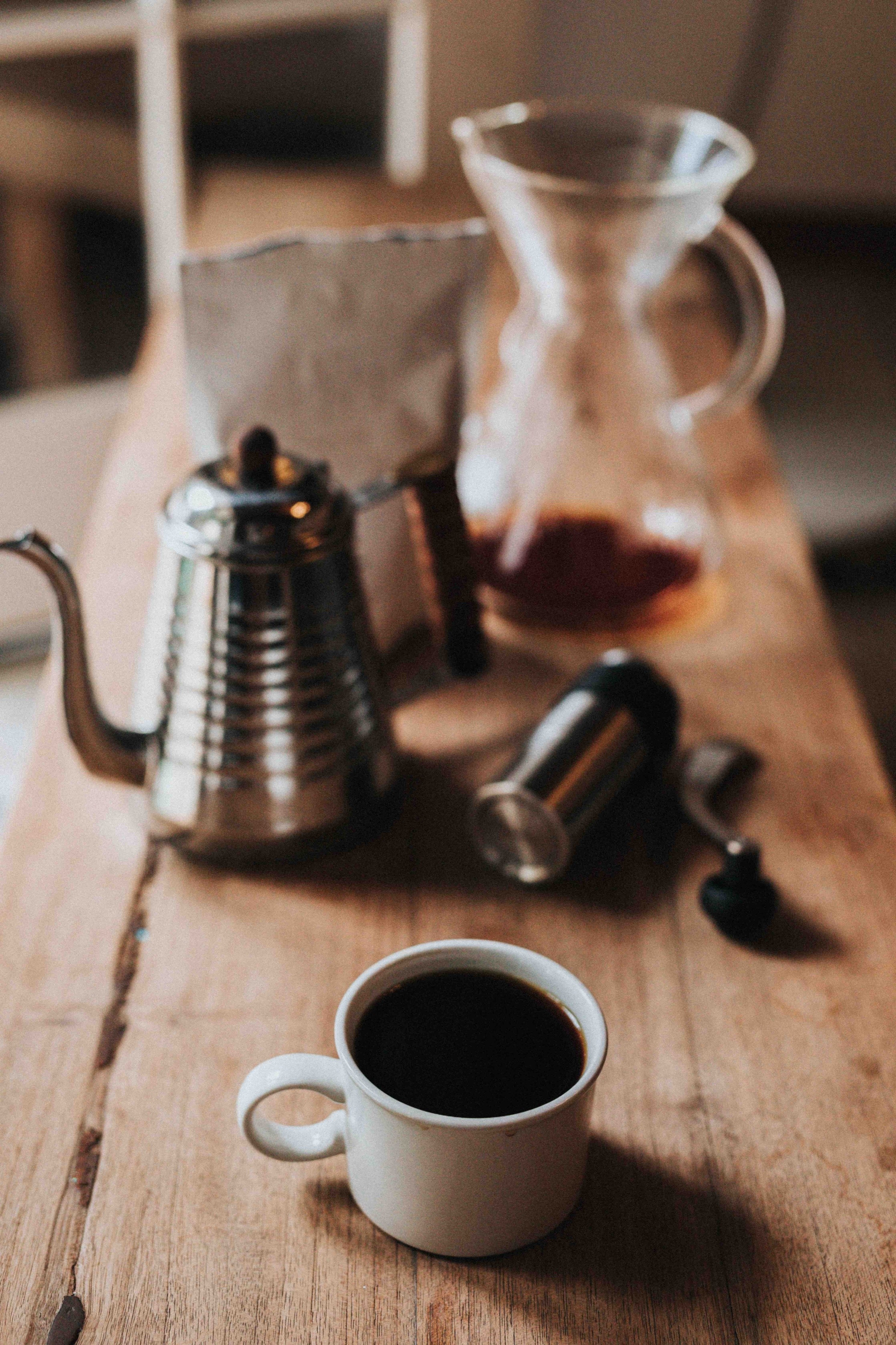A Chemex brewer, a goose-neck kettle, a hand burr grinder, and a mug of coffee.